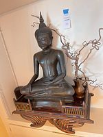 Overall view of bronze Buddha figure seated on wooden stand with copper pitcher and natural twig