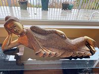 Full view of reclining Buddha sculpture showing its size and posture on a glass table.