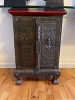 Front view of one cabinet showing metal overlay doors with seated Buddha motifs and red stained top