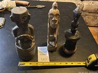 Three carved African statues of varying sizes side by side with measuring tape showing length.