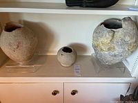 Wide view showing all three artifacts displayed on clear stands on a white cabinet shelf