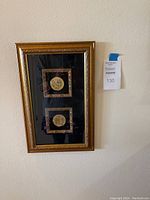 Two gold-toned Bahrain coins framed vertically in an ornate gold frame against black backing.