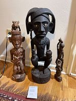 Three statues side by side on hardwood floor against white wall.