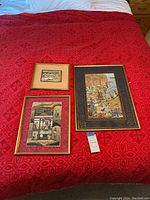 Three framed Middle Eastern prints displayed on a red bedspread showing the varying sizes and gold-toned frames.