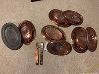 Disassembled oval copper containers and lids with two metal locking handles.