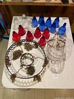 Top down view showing multiple colored glass bell jar pieces in red, blue, and clear with metal chandelier frame and chains on white cloth.