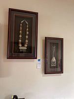 Two framed items hanging on wall, a larger necklace on the left and smaller pendant on the right.