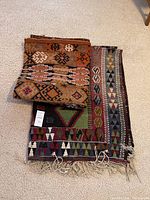Two kilim style rugs stacked, showing colors and patterns of both.