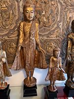 Full view of both gilded Buddha statues against a tapestry background