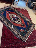 Two rugs stacked on a floor with furniture around