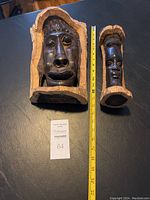 Two wood carved African faces with tape measure for scale, showing size difference