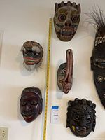 Overview of six carved masks mounted on wall with measuring tape alongside