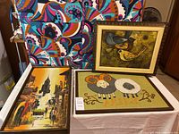 Four items in the lot include a colorful folding floor mat and three framed artworks displayed on a table.