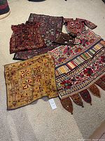 Full view of six embroidered textile pieces laid out on floor including vests, rectangular cloth and decorative panels