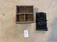 Wooden nut box with three compartments next to carved wooden panel shown on carpet floor