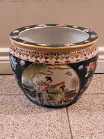 Front view of the Asian decorative planter showing detailed painting of two traditional figures in a nature scene with gold accents at the top edge.