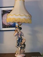Full view of the Italian traditional boy ceramic lamp with fabric shade and gold fringe.