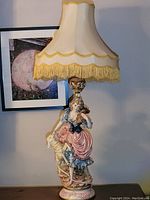 Full view of the Italian traditional girl ceramic lamp with fabric shade and gold fringe.