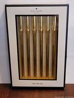 Front view of Kate Spade Strike Gold Pen Set box containing 6 gold pens in clear window packaging.