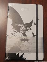 Front of new Moleskine Batman notebook sealed in shrink wrap showing Batman embossed imagery, black elastic band, and logo.