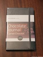 Front view of new Moleskine Chocolate Journal in black with chocolate bar embossing and product band showing title and branding.