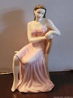 Front view of the porcelain figurine showing seated woman in a flowing pink dress with bow details, legs crossed, and resting an arm on the chair back.
