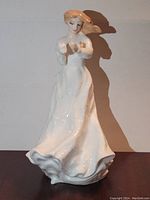 Front view of white ceramic figurine of a woman with brown hair in flowing dress holding an object.