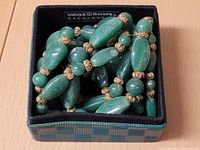 Top view of densely strung solid jade beads of different shapes placed in a small black and green checkered box.