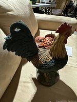 Full view of the ceramic rooster figurine from the side showing detailed feather painting and base decor.