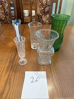 Five glass vases displayed on wooden table, various shapes and sizes, front view showing details and colors
