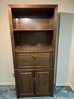 Front view of the wooden shelving unit showing open shelves, drawer, and cabinet doors at base