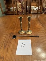 Two brass candle sticks and a brass candle snuffer arranged on a wooden table showing full set.