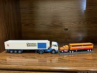 Side view of two collectible toy trucks, Christian Salvesen truck with white and blue refrigerated trailer and smaller Horse Brass orange-black trailer.