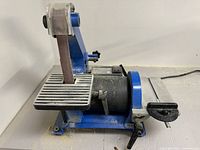 Side view showing the vertical belt sander with metal work rest and blue frame.