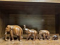 Four wood elephants of different sizes aligned on a wooden shelf.