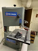 Front view of King Canada electric band saw showing brand label, large work table with measurement grid, and blade area with protective guard.