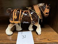Side view of the ceramic horse showing glossy brown and white body with leather harness and metal chain detail.