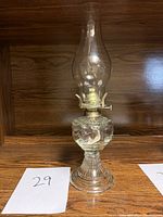 Full view of the vintage oil lamp showing its tall glass chimney, ornate glass oil reservoir, ribbed pedestal base, and metal wick burner.