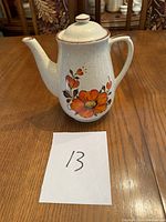 Front angle showing the teapot with orange and red floral patterns, lid on top, white card with '13' in front.