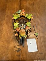 Front view of clock with pinecone weights, pendulum, and carved leaf and bird details