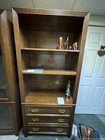 Front view of the shelving unit showing three open shelves and three drawers at the base, with wood grain visible and hardware in place.