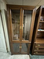 Full view of the tall wooden shelving unit with upper and lower glass doors, brass handles, and wooden frame with detailed grooves on the sides.