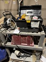 Wide view of metal tool trolley with items including circular saw, toolbox with smaller tools, containers on shelves.