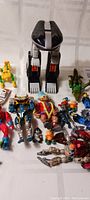 Various used toy action figures including large black and silver robot, red mechanical dinosaur, green dragon figure, multiple humanoid figures in blue, red, and flesh tones.