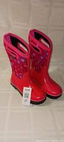 Full view of the pair of bright pink and red BOGS youth winter boots with decorative floral pattern and barcode tag
