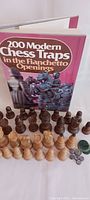 Chess book '200 Modern Chess Traps in the Rianchetto Openings' with wooden chess pieces arranged in front.