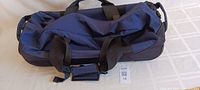 Photo showing the top and side of the blue duffle bag with black carry handles and shoulder strap.
