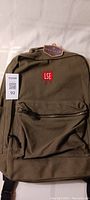 Olive green Oakdale Daily backpack with LSE logo patch and tags attached, shown hanging.