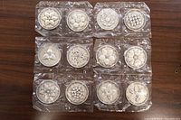 All 12 medals sealed and laid out showing the front sides depicting Canadian provincial flowers.