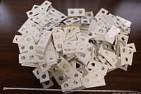 Overview of a large pile of white cardboard coin holders with circular cutouts for coins, displayed on a table with measuring tape.